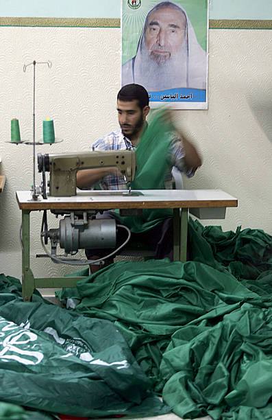 فلسطيني يخيّط أعلام  حsاس في مصنع للخياطة. وخلفه صورة للشـ ..هيد أحمد ياسين.
مدينة غزة، قطاع غزة– 10/8/2005