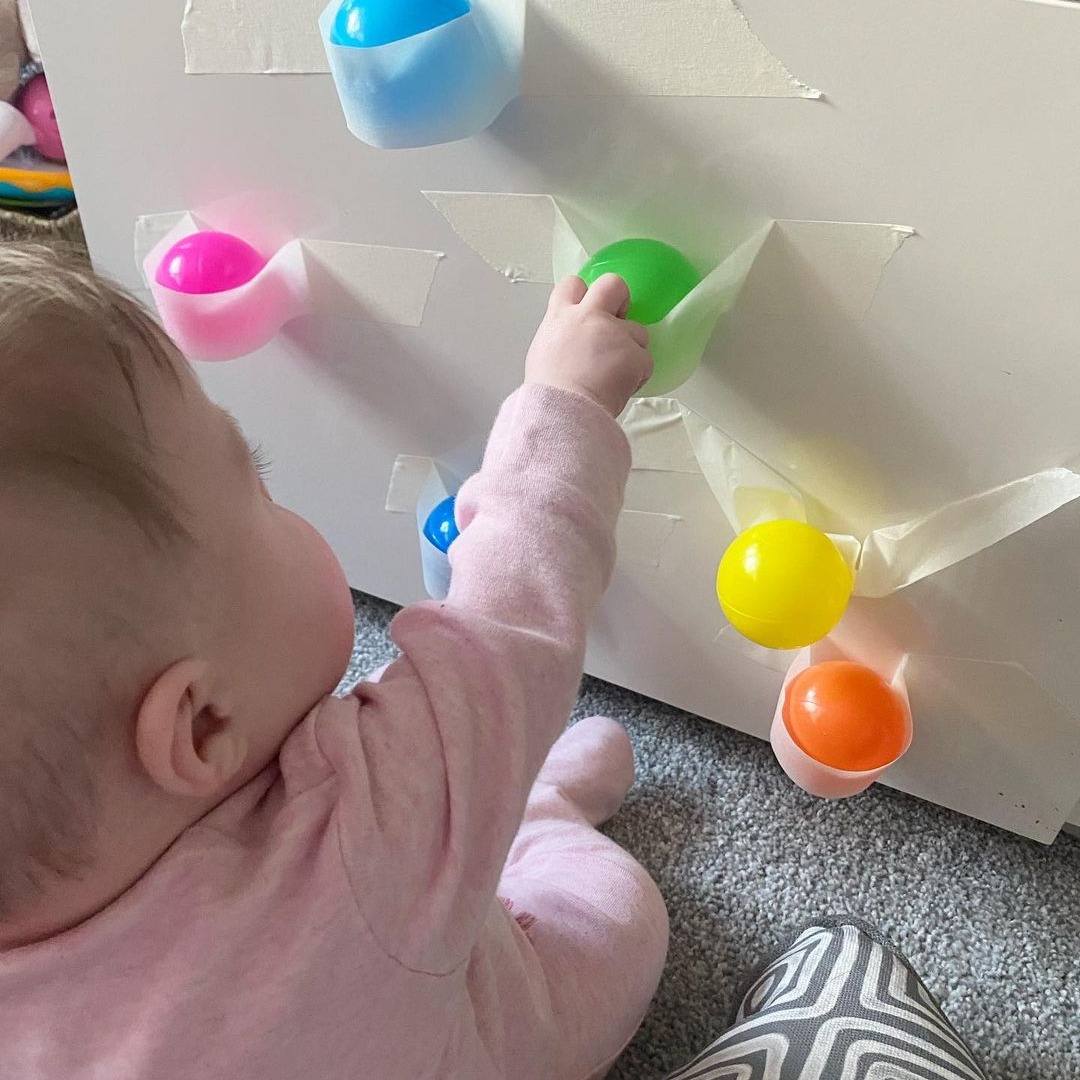 Develop baby's fine motor, hand-eye coordination, and balance skills from 7 months of age! Tape plastic balls to a wall using painter's tape and watch baby try to pull off the tape to get the prize. Play 7-9 month baby games: pathways.org/growth-develop… Via play.develop.discover