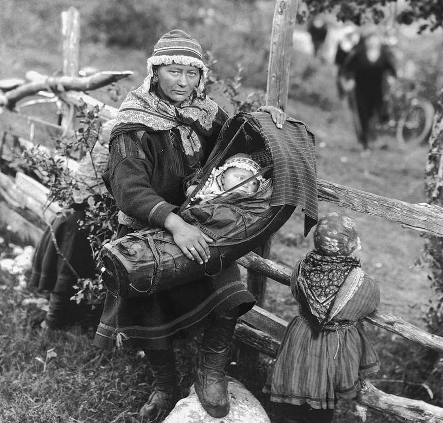 A Sami woman photographed standing by a wooden fence with her children in Lyngen, Troms, in c. 1925. Photograph taken by Anders Beer Wilse. The Sami people are a Finno-Ugric people inhabiting Sápmi,