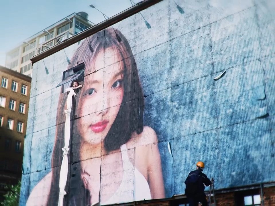 Nayeon's unit location is cleverly placed, creating an illusion of the makeshift bed sheet rope as a hair accessory for the giant ads Nayeon