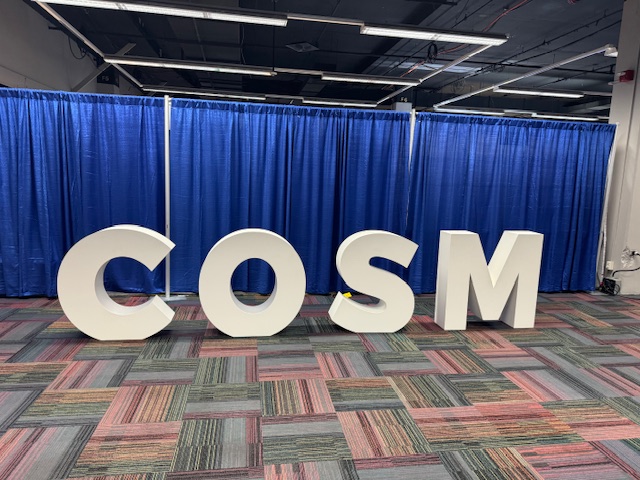 #2024COSM COSM photo opportunity by the posters in the Riverside Exhibit Hall.