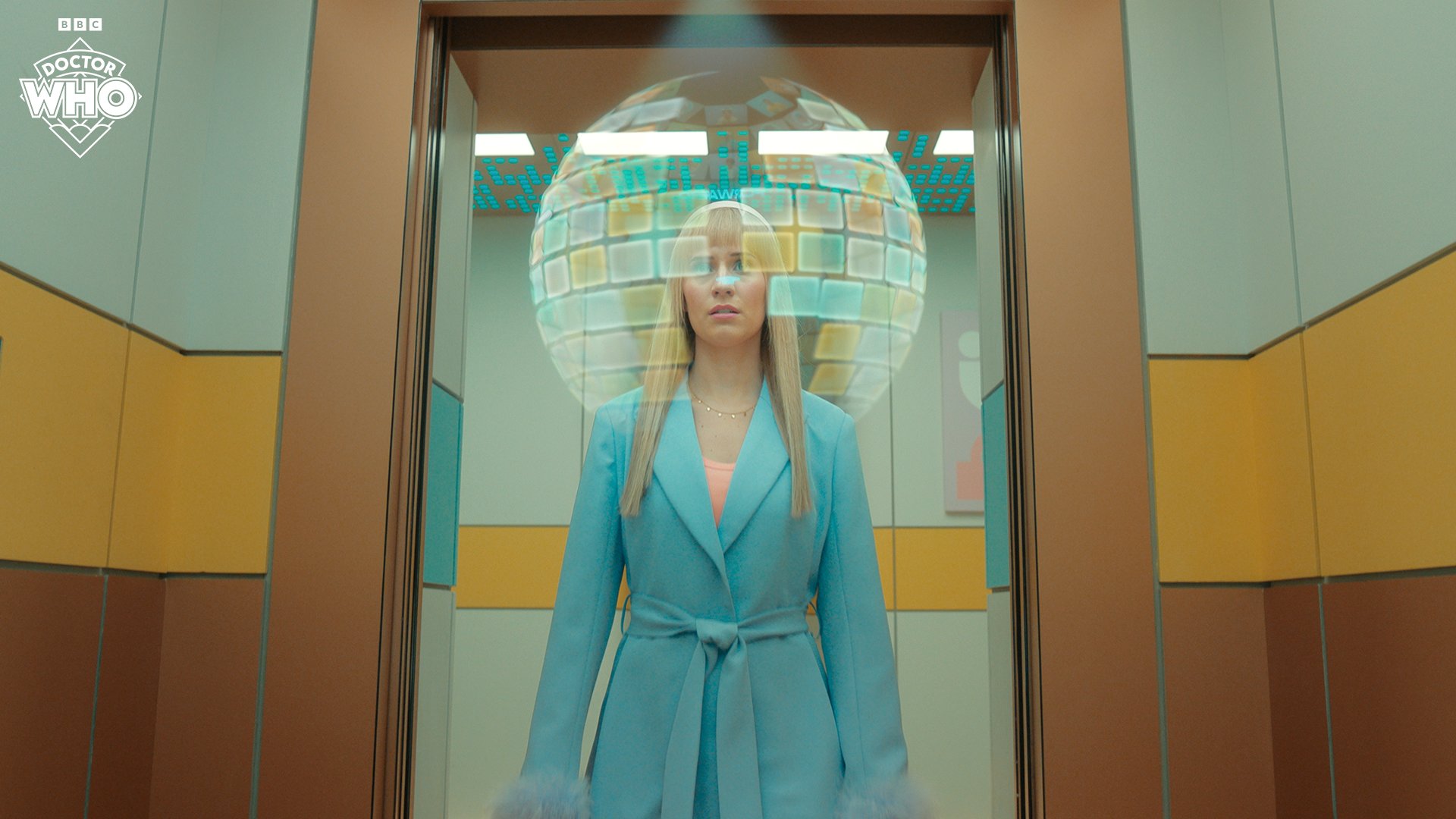 Callie Cooke as Lindy Pepper-Bean in 'Dot and Bubble'. She is standing in an elevator doorway with a sphere of small screens around her head.