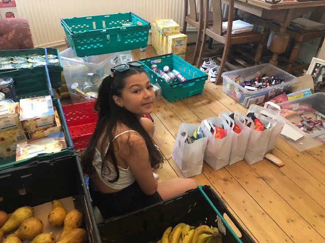 A young girl sitting on the wooden floor in a house helping to pack snack bags