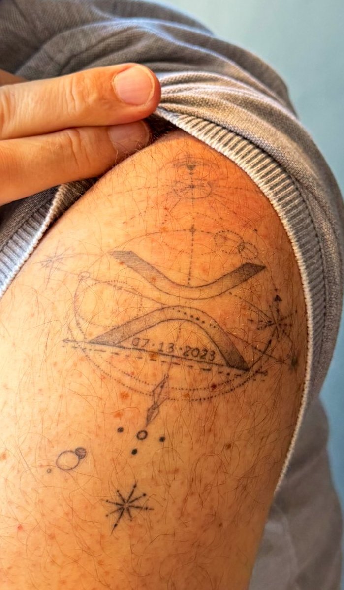 Tattoo of Brad Garlinghouse : The logo of the XRP is in the completed  circle, and six planets are aligned in a straight line through its center  6/4 6 planets + the