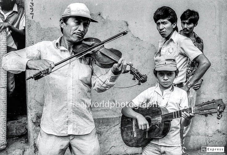 A father and son play the mean streets of Guatemala City, Guatemala, Central America. 1992. Gary Moore photo. Real World Photographs. #blackandwhitephotography #guatemala #music #streetphotography #photojournalism #garymoorephotography #realworldphotographs #photography