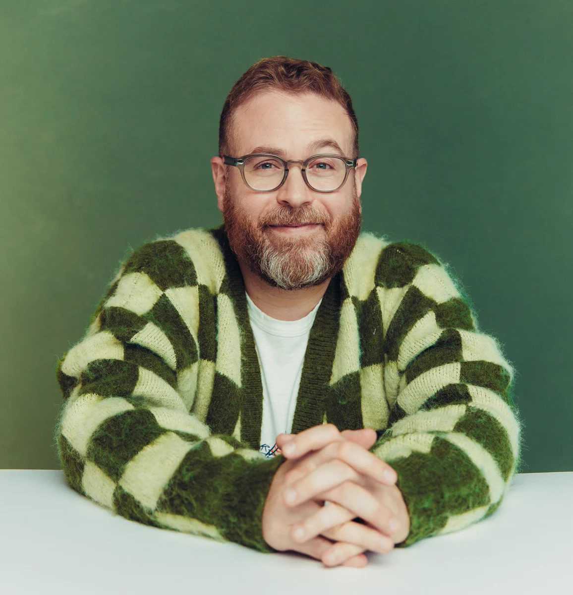 Sam in studio in a green checkered cardigan against a green backdrop, looking like the frog he is.