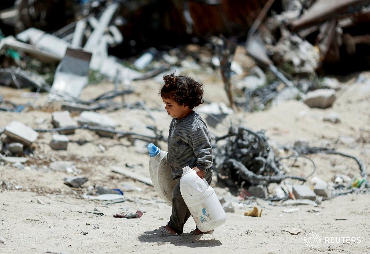 A Palestinian girl carries cans to collect water as she walks by houses which were destroyed in an Israeli strike, amid the ongoing conflict between Israel and Hamas, in Khan Younis, in the southern Gaza Strip, May 22, 2024. REUTERS/Mohammed Salem