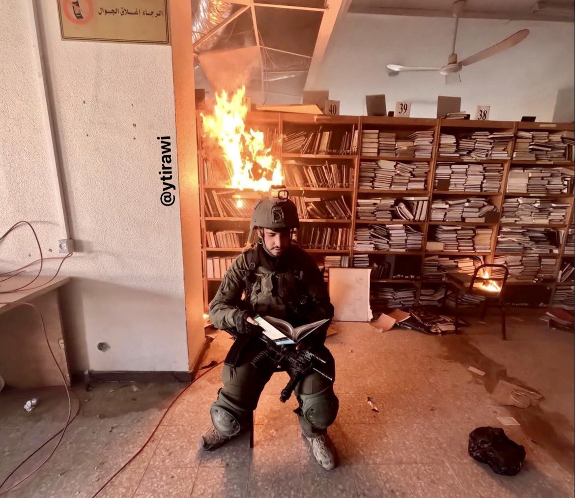 🔴Des soldats israéliens ont incendié la bibliothèque de l'Université Aqsa située dans la ville de Gaza, un des soldats se met en scène en mimant de lire un livre et se prend en photo avec comme arrière plan des livres en flamme.