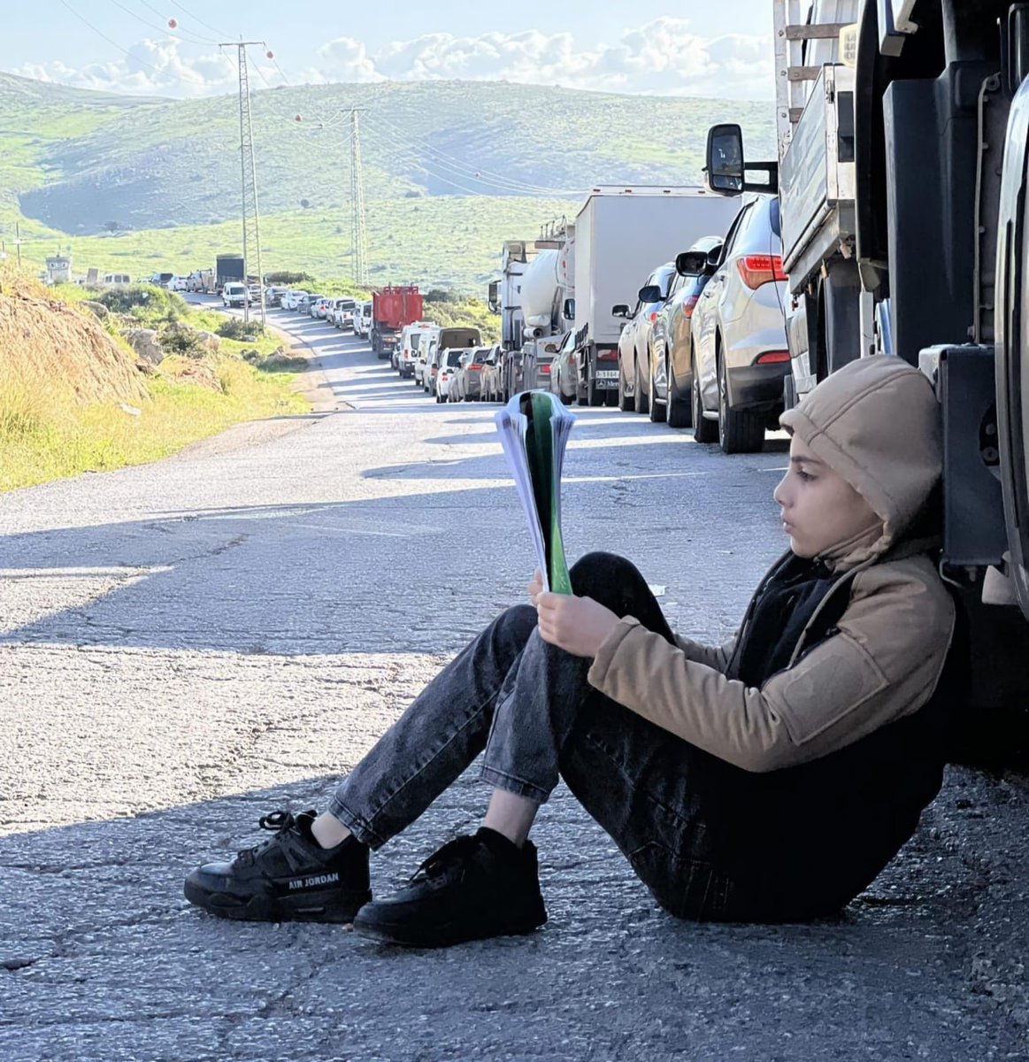 QudsNen's tweet photo. A Palestinian school student reads while waiting for the Israeli checkpoint to open, allowing Palestinians to leave their villages and towns in Tubas, occupied West Bank. https://t.co/m7gd3GqfbK