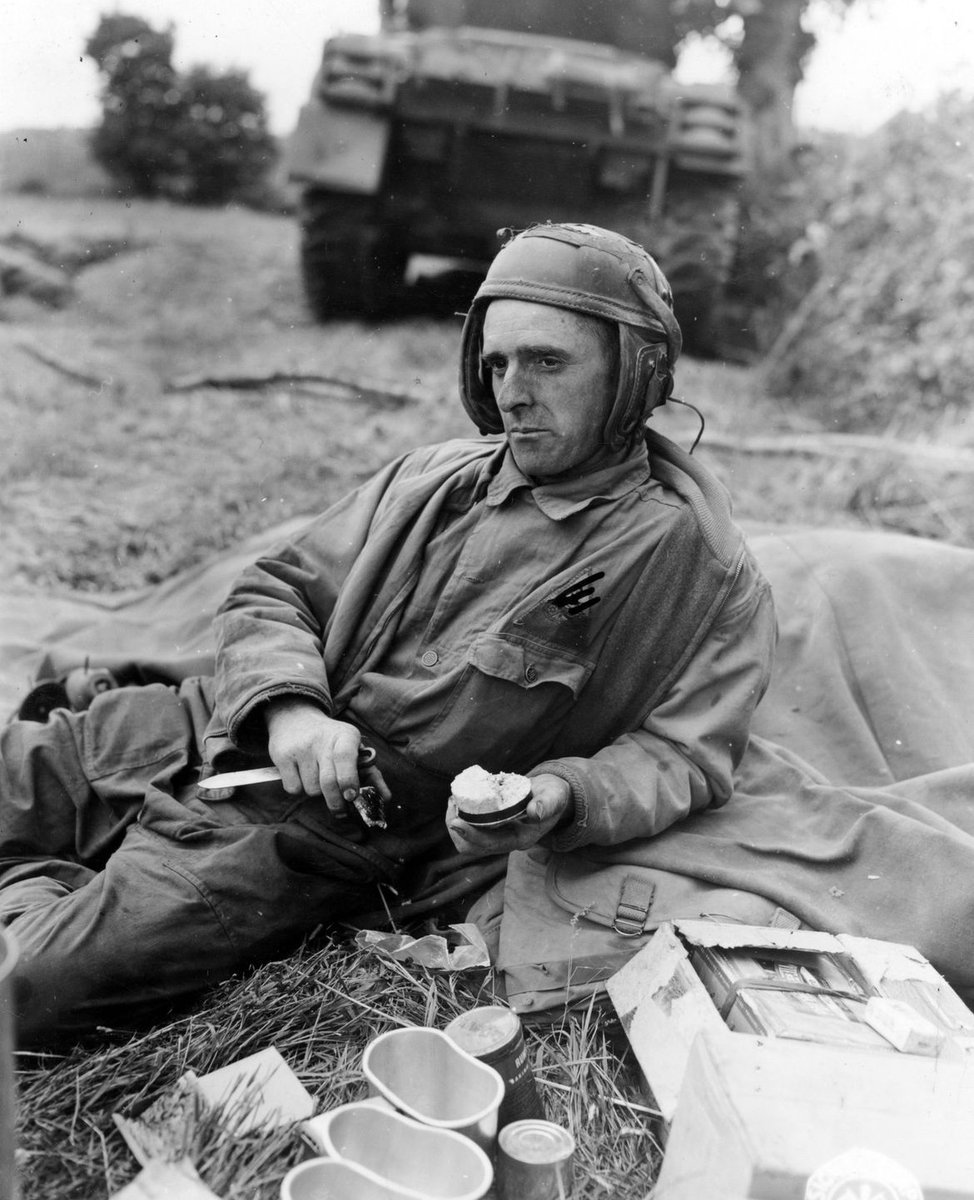 During a lull in fighting, Pfc. Jerry Coleman, an assistant tank driver with the 3rd Armored Division, takes some time out to eat his K Rations near Saint-Jean-de-Daye, France. 🪖