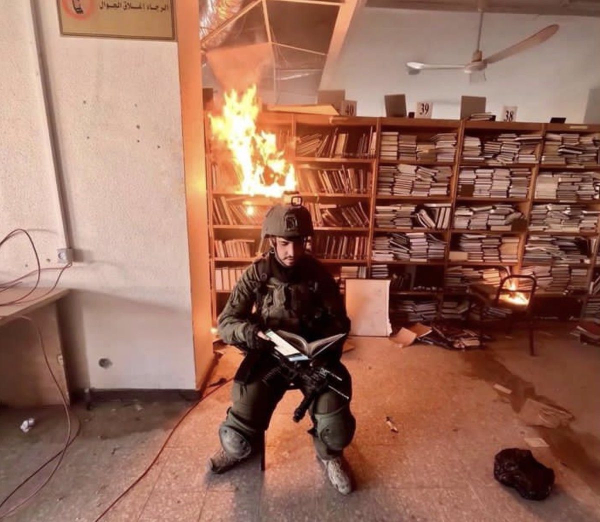 Ein israelischer Soldat posiert in der Bibliothek der Al-Aqsa-Universität in Gaza, nachdem er die Bücher im Brand gesetzt hat.

Die Bibliothek wurde vollständig niedergebrannt. Israels Armee hat alle 12 Universitäten in Gaza systematisch zerstört. Bücherverbrennung passt zu den