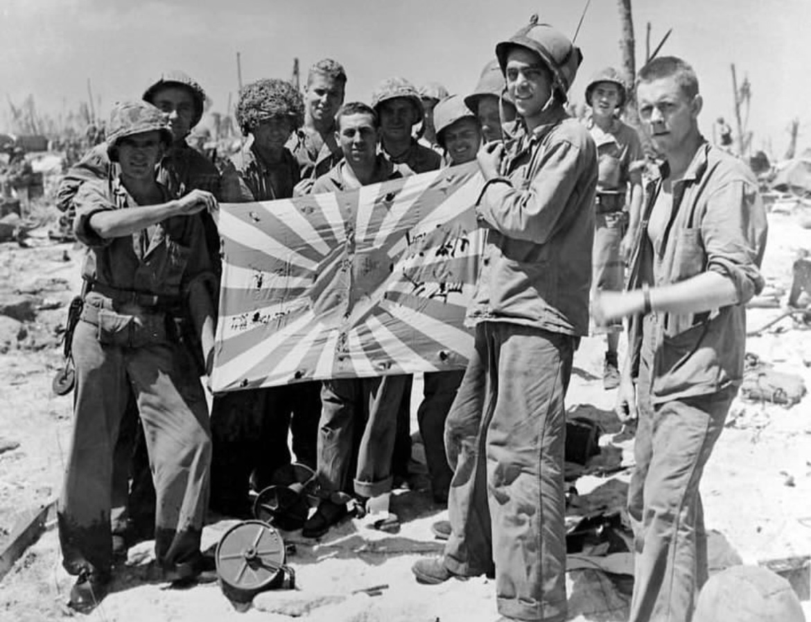 In February of 1944, Marines of 22nd Marine Regiment display a captured Japanese flag, picked up by one of them during the capture of Engebi Island in the Eniwetok Atoll. 🪖