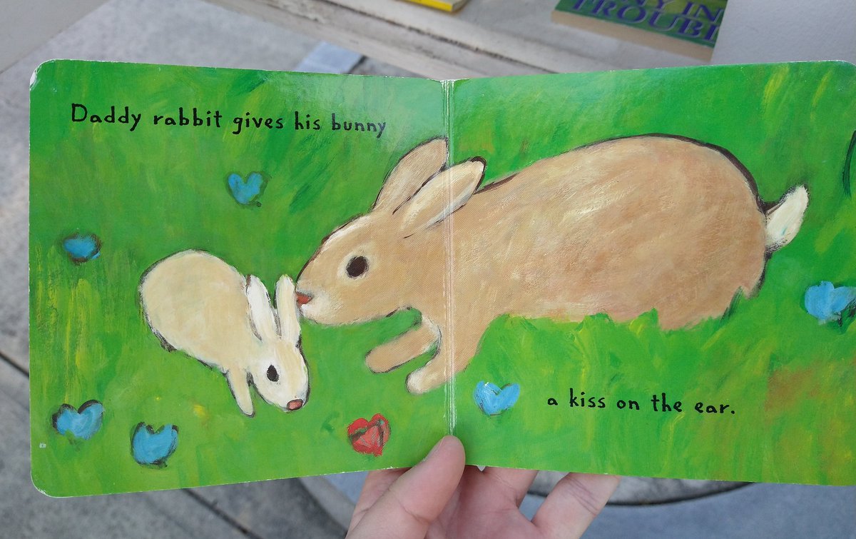 Interior pages of picture book. Illustration of an adult rabbit touching its nose to a baby rabbit. Text reads "Daddy rabbit gives his bunny a kiss on the ear."