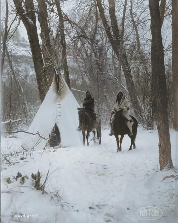 Two Apsaroke Native Americans on horseback outside of a tipi in a snow-covered forest in Montana in 1908. Credit: anton_colorization