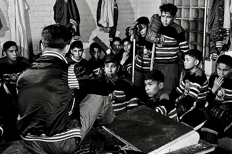 Dressing room meeting of the Black Hawks, from the Pelican Lake Residential School, during their 1951 tour of Ontario, including Maple Leaf Gardens. “We were sneaking down at four in the morning... just to skate around the rink and play hockey” - (late) Chris Cromarty.  1/2