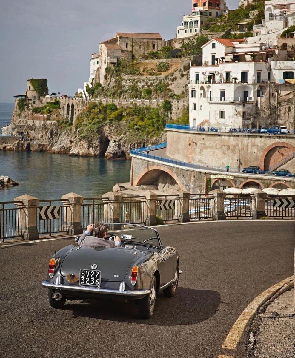 A 1963 Alfa Romeo Giulia Spider winds along the Amalfi Coast with class.