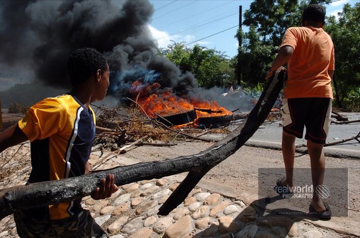 Protesters fan a fiery roadblock in Pedernales, Dominican Republic. Gary Moore photo. Real World Photographs. #world #photojournalism #dominicanrepublic #editorial #garymoorephotography #realworldphotographs #history #protest #poverty #roadblock #images #stock #people #places