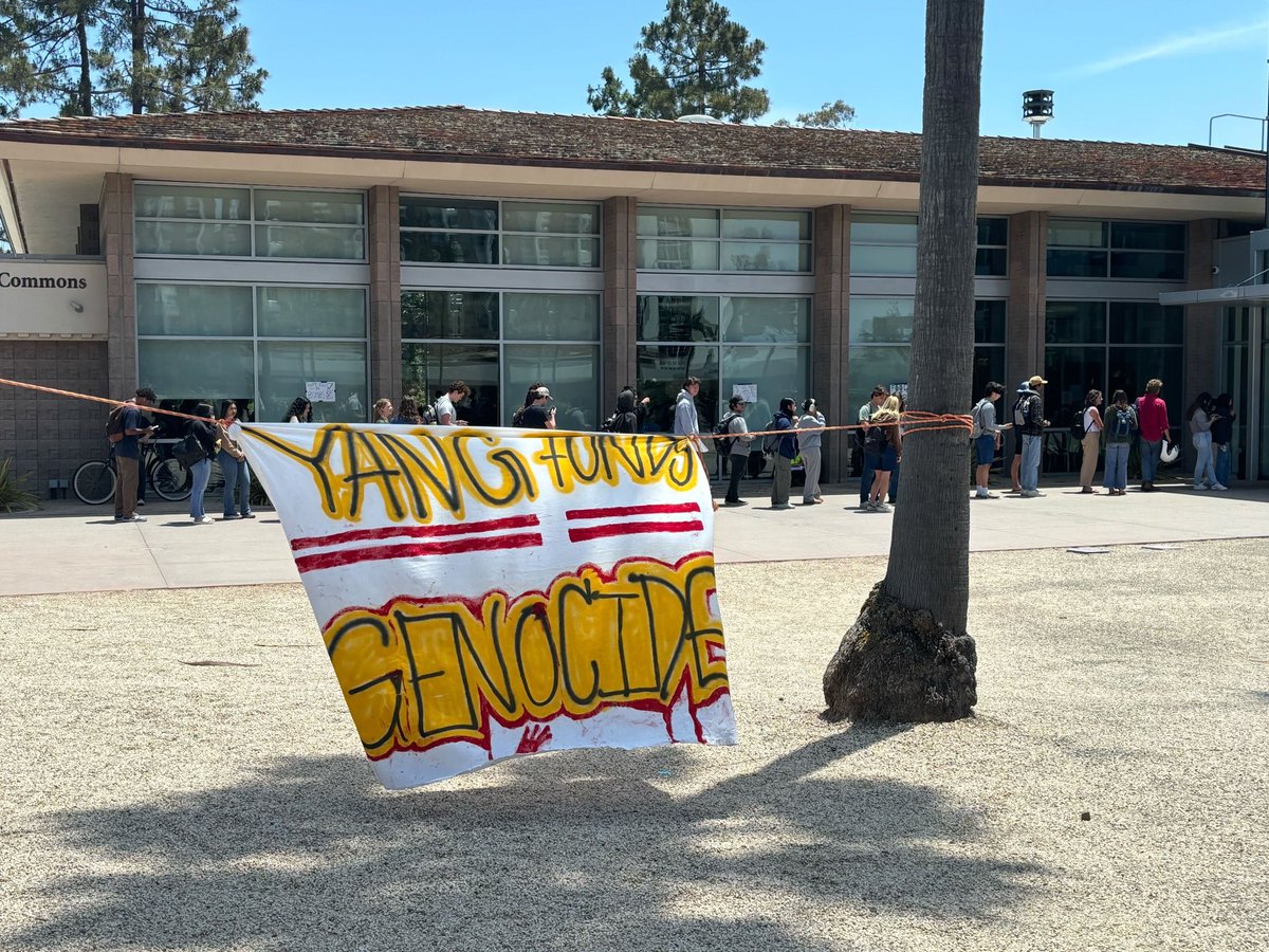 dailynexus's tweet image. Signs outside DLG read “Food not Bombs” and “Yang funds genocide,” among others. Two legal observers in neon yellow vests stand outside the DLG entrance, looking out for instances of police brutality to report to the National Lawyers Guild, one observer told the Nexus.