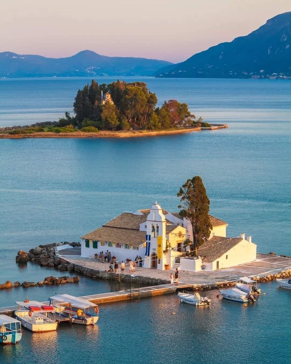Good morning from Corfu! The sun is painting the sky. Standing on a peninsula, I'm looking out at a charming little church overlooking a calm harbor with a few boats bobbing gently. In the distance, the tiny island of Pontionisi adds to the magic. #Greece #Corfu #IslandLife