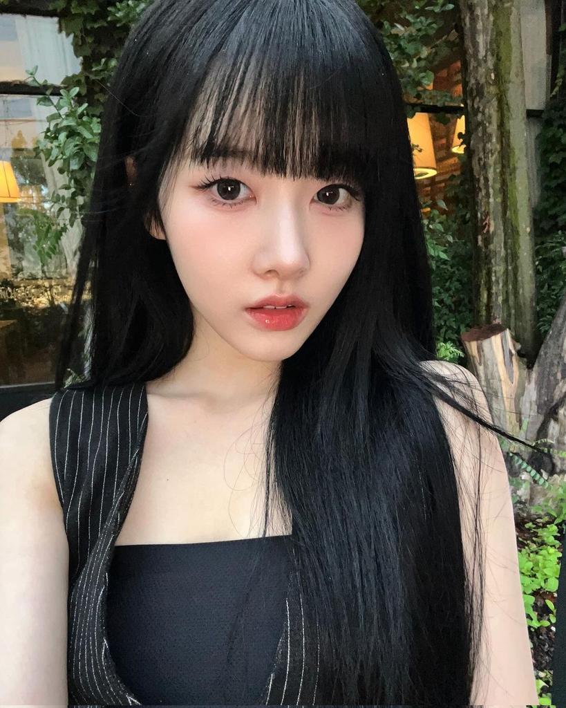 Her eyes, deep as twilight's hush, gaze into the soul, while the surrounding greenery frames her with nature's tender embrace.