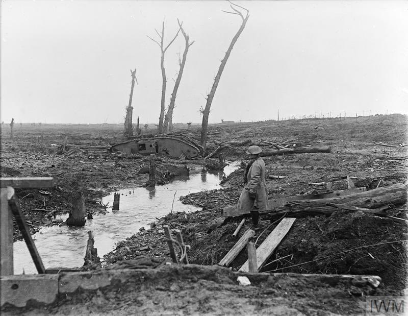 Views of the battlefield after the third Battle of Ypres, 1917. A soldier look across devastated country near Ypres showing a derelict Mark IV Tank, shell-splintered trees and general battle detritus, 15 February 1918. IWM Q 10711