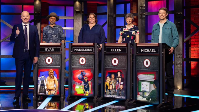 Tom Gleeson with four contestants on Hard Quiz. Topics on the screens are the Carlton Football Club, sci-fi show Babylon 5, Otzi the Iceman, and Microsoft Excel.