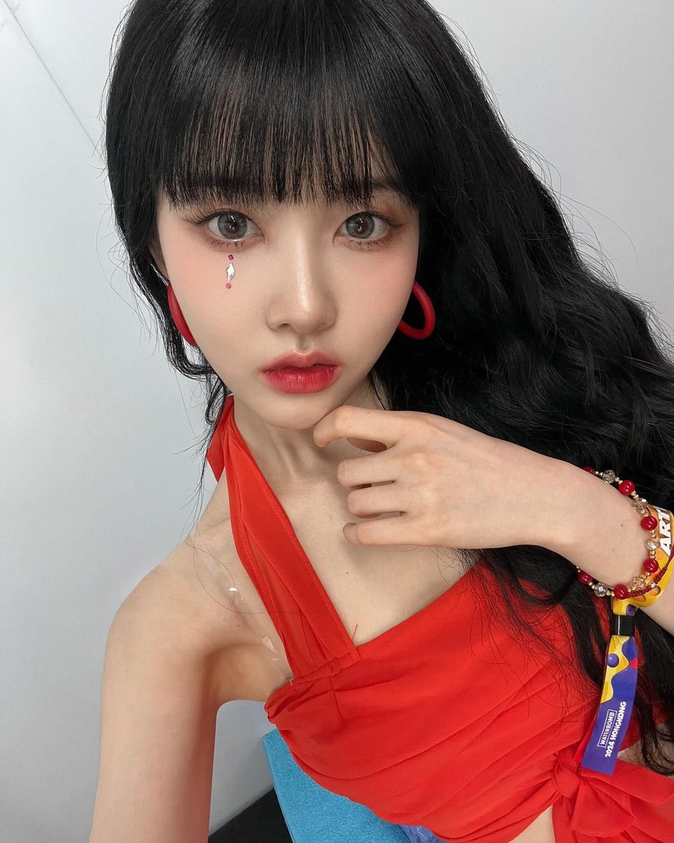 In a moment of delicate grace, she gathers her midnight tresses, her vibrant crimson attire echoing the fierce passion within her soul, as tears of glitter trace the contours of her serene visage.