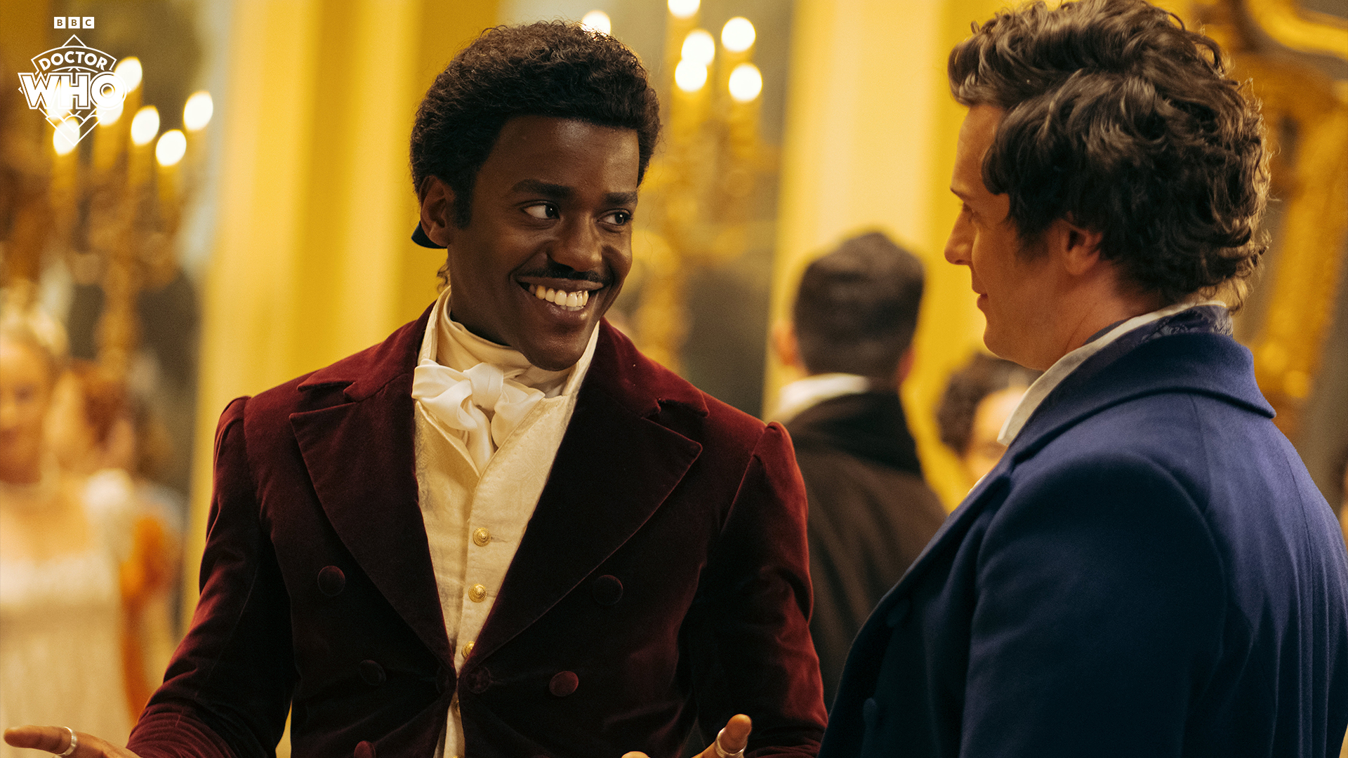 This is a close up of Ncuti Gatwa as the Doctor in a Regency outfit. He is smiling and looking at Rogue played by Jonathan Groff.