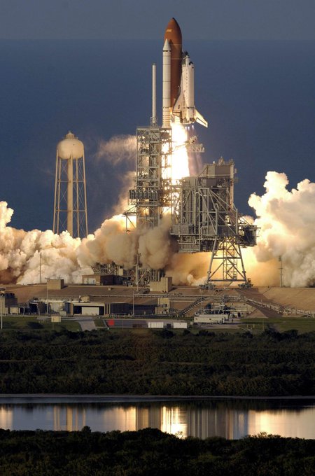 A close range shot of a space shuttle launching from a launch pad while attached to a large ignited rocket.