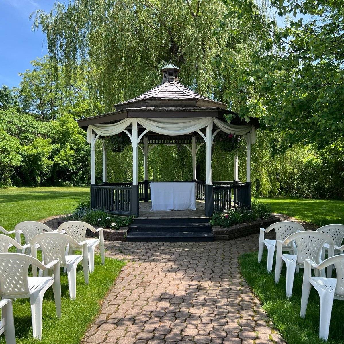 Our grounds feature manicured lawns and landscaped gardens, framed by a lush weeping willow in the back. The stone patio leads to our picturesque gazebo, the perfect setting for the exchange of vows during warm seasons — a pinnacle moment for you and your guests.