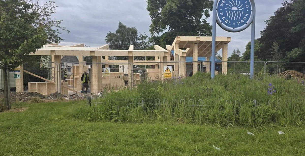 A building site in the background shows a wooden structure halfway through construction with columns and parts of the roof visible.