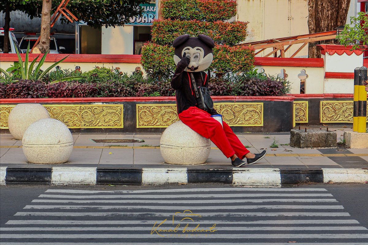 budislank87's tweet photo. "Karakter Kartun Duduk Santai di Trotoar Kota"

Di tengah hiruk-pikuk kota, seorang individu mengenakan kostum karakter kartun terkenal duduk santai di trotoar. Dengan latar belakang ornamen berwarna emas yang kaya detail dan tanaman hijau, karakter ini memberikan sentuhan ceria. https://t.co/UmIuaJaB4G