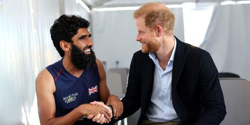 Wali Noori - a blind Afghan refugee - wears a British athletics kit and sits next to Prince Harry. They are facing each other shaking hands with broad smiles on their faces.
