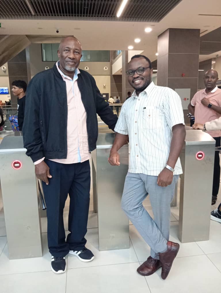 Umoja Conservation Trust (UCT) Trustee Bryan Toshi and Prof Frank Mugyenyi  ED Minerals for Africa Development Initiative (Madi) pause for a photo at the Tz Electric Train Station on their way to present a paper on 'Sustainability in Mining' at the Tanzania Mining Week 2025.