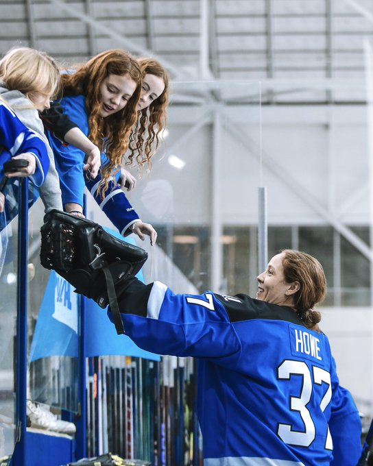 A photo of Erica Howe handing young fans a puck after a game.