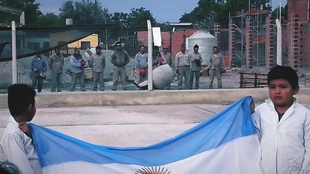 Salta, frente al colegio Pichanal. Un grupo de obreros de la construcción detiene su tarea para honrar la ceremonia de izamiento de la bandera de los pibes. Un docente, Hipólito Ayala, captó la imagen. MI PAIS 🛐🇦🇷♥️