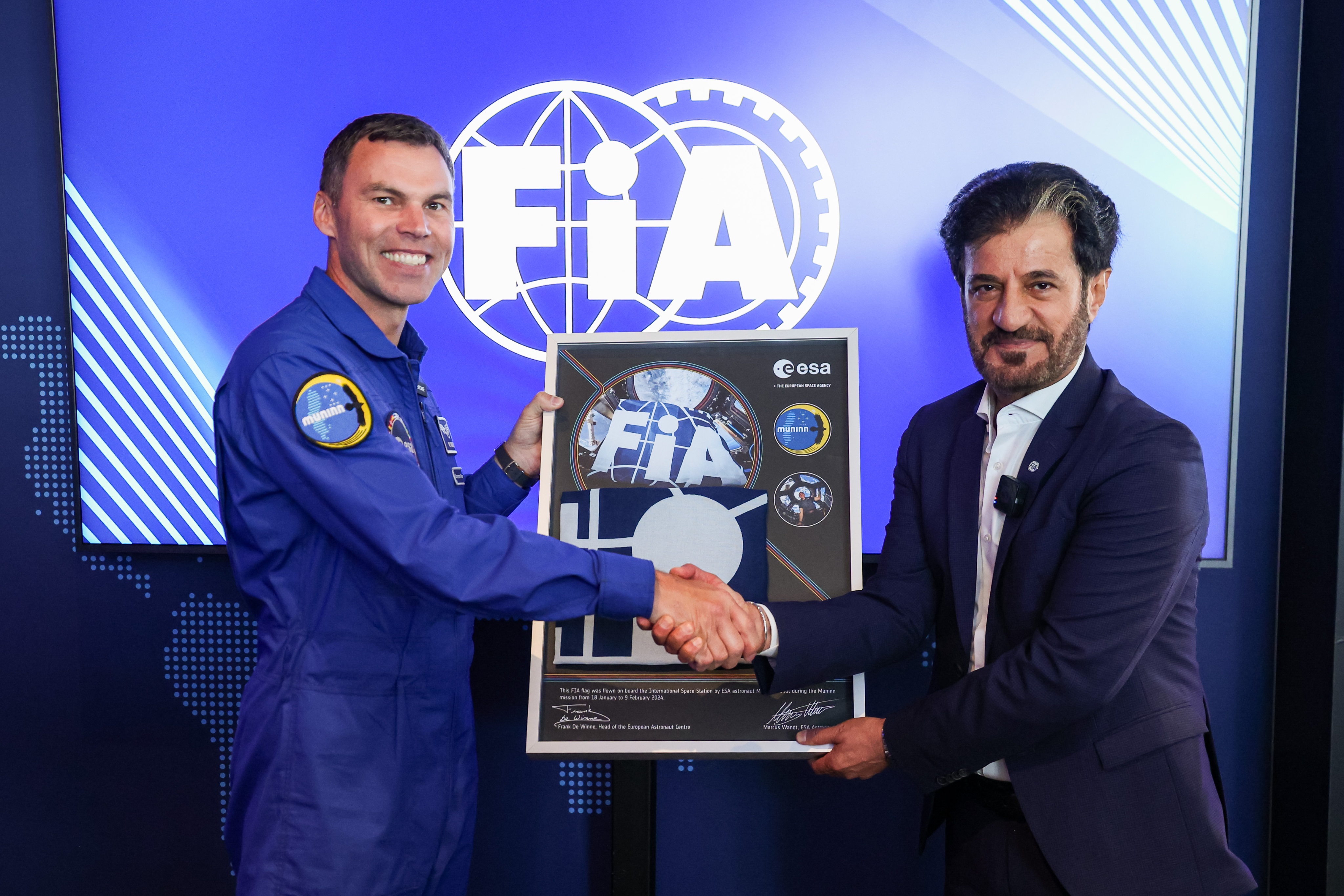 ESA astronaut Marcus Wandt in blue flight suit (on left) presents FIA President Mohammed Ben Sulayem with a FIA flag he carried to the International Space Station earlier this year to mark the Federation’s 120th anniversary. 