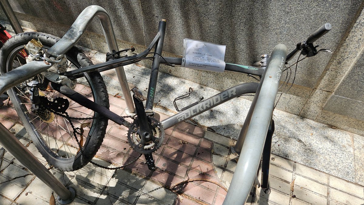 Junto al Corte Inglés. Esto no es un 'vehículo', como dice la Policía en el aviso, es un escombro. Llévensela ya y arreglen el aparcabicis para que se pueda usar. Si acaso, pongan una pegatina como hace la grúa cuando retira un coche y el dueño, si aparece, que vaya al depósito