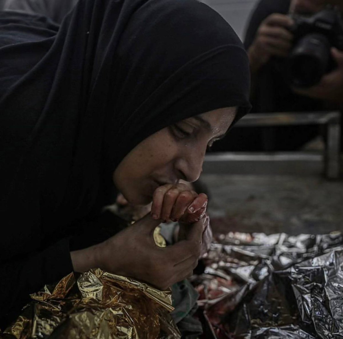 Seorang ibu Palestina mencium tangan putrinya yang tewas dalam pemboman Israel di kamp Bureij.
