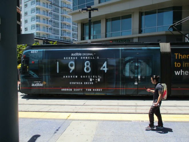 SD_Comic_Con's tweet photo. Big Brother is watching. @coolsandiego caught a glimpse at a new @sdmts trolley wrap for @audible_com originals #1984 and #TheSafeMan:  https://t.co/bjGBiezhYe https://t.co/gz836VQcLh