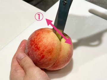 桃のヘタ（上）側に十字の切れ込みを入れているところです。