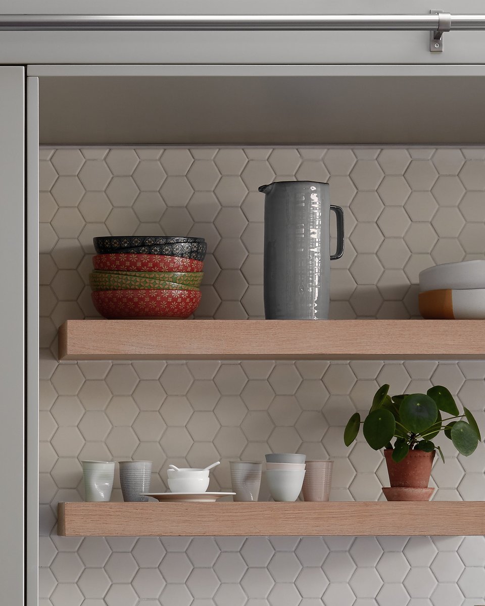 Clean lines and hexagon tiles for Yam Studios in Elle Decoration magazine. Grey cupboards and wooden textures compliment the soft light falling through the skylight. Pomegranate on a wooden chopping board in front of stacks of bowls and a coffee pot.