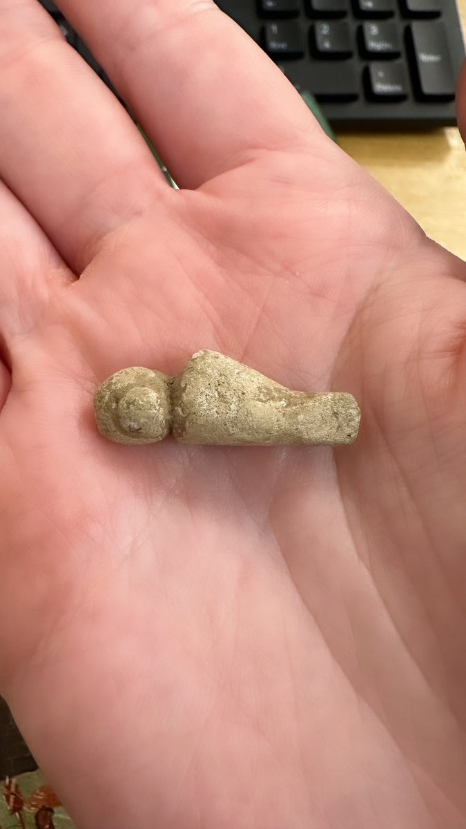 Appeal to anyone and everyone: what the heck is this little figurine?

Made of lead, solid cast, flat on one side, crudely incised face and hair in a bun. Diagonal base does not seem broken. Looks like an owl person. 

Baffled again! 😩

#FindsFriday #AskAnArchaeologist