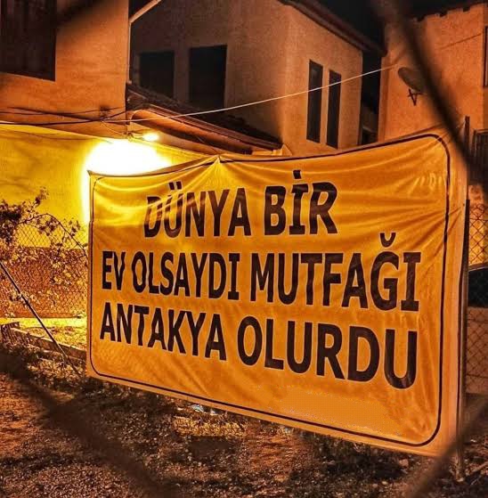 siyahkartus's tweet photo. Eski Antakya'nın girişinden bir pankart... İlk gördüğümde gururlu bir şekilde gülümsemiştim. Deprem bizden her şeyimizi aldı ama dünyanın mutfağı hala yerli yerinde duruyor. https://t.co/WWkFUGi6iK
