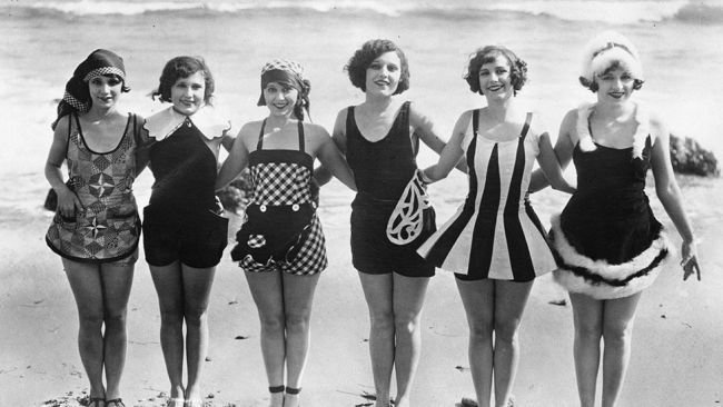 A group of women showing off some unusual and original swimwear on the beach. Photographed in 1929.