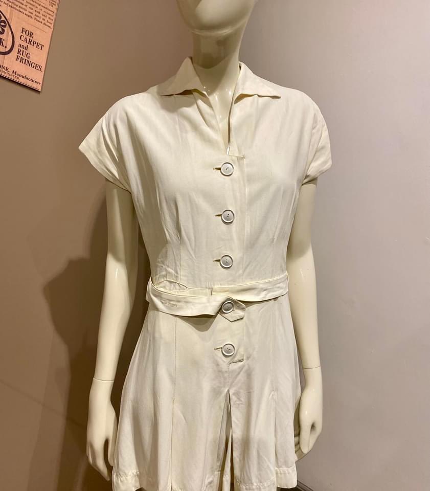 MuseumofCarpet's tweet photo. Playful piece from our 1940s display! Not quite vintage Wimbledon but not far off!  A cream button-fronted badminton outfit, faux silk, divided skirt &amp; pocket on the right. Standing on a first piece of carpet from loom with double grippers, Brintons Ltd, Gripper Axminster, 1946 https://t.co/4uIhLcAmuv