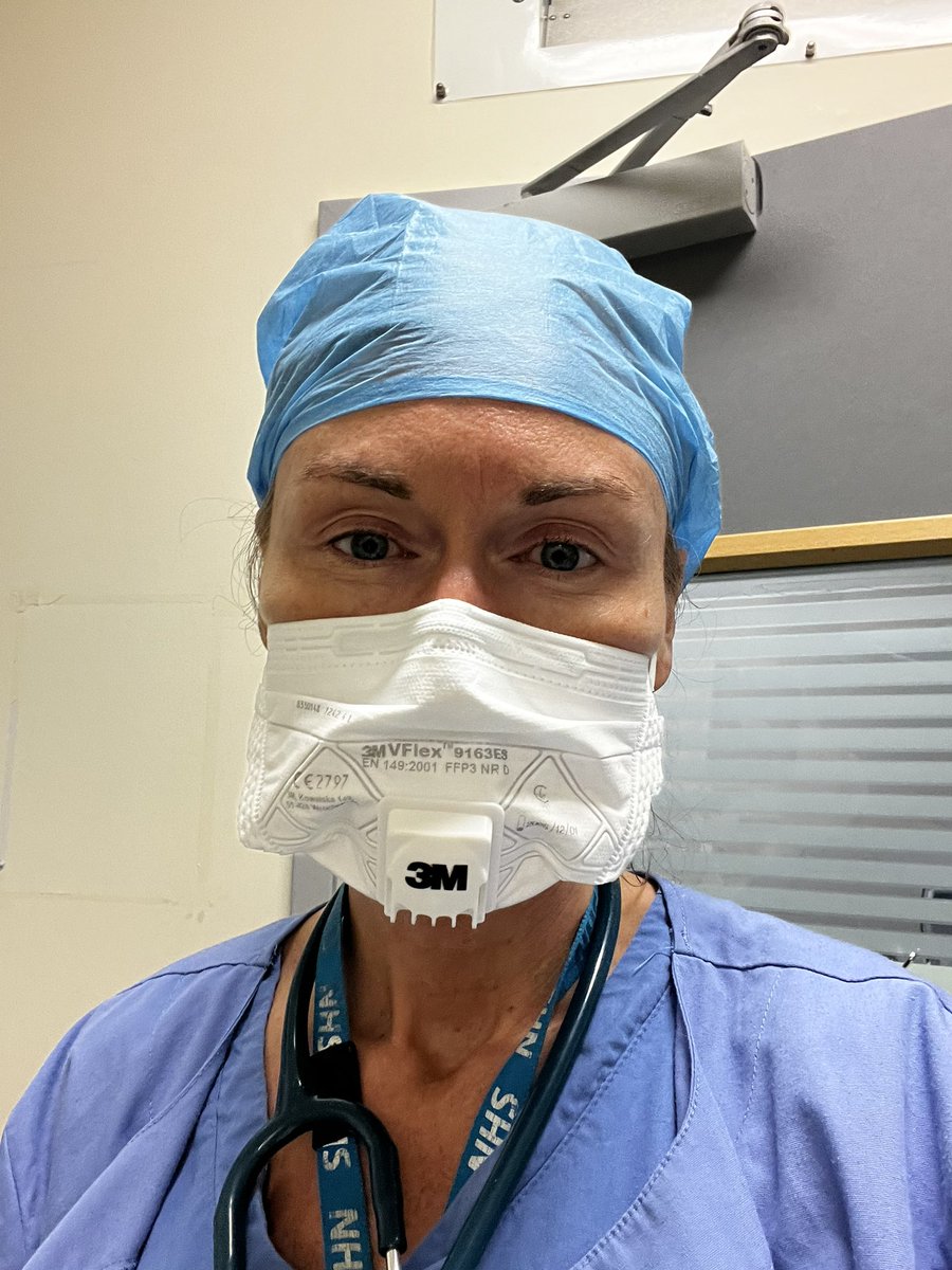 Selfie of Linn wearing scrubs, hat, and an FFP3 mask with a stethoscope and lanyard around the neck.