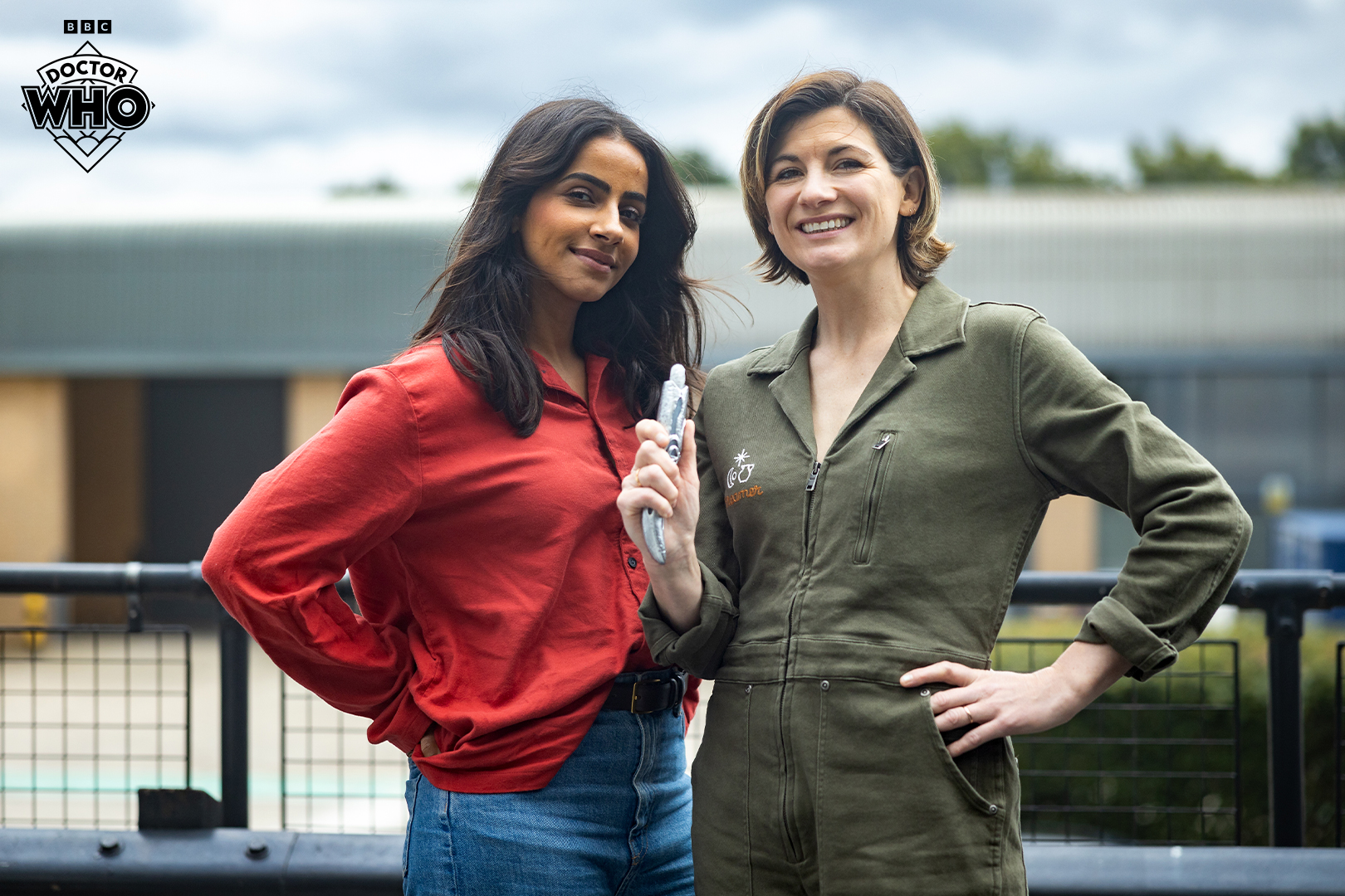 Mandip Gill (Yasmin Khan) and Jodie Whittaker (the Thirteenth Doctor) pose for a photo outdoors. Jodie is holding the Thirteenth Doctor's sonic screwdriver.