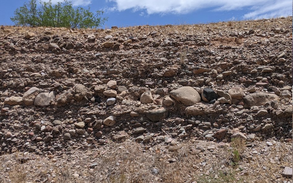 Coarse-grained, poorly-sorted alluvial fan deposits (fanglomerate) exposed  along US 191 near 3 Way, AZ, in Greenlee County (32.95016N,  -109.227777 W). Note the train of coarse, well-rounded cobbles and boulders in the  center of the photo.