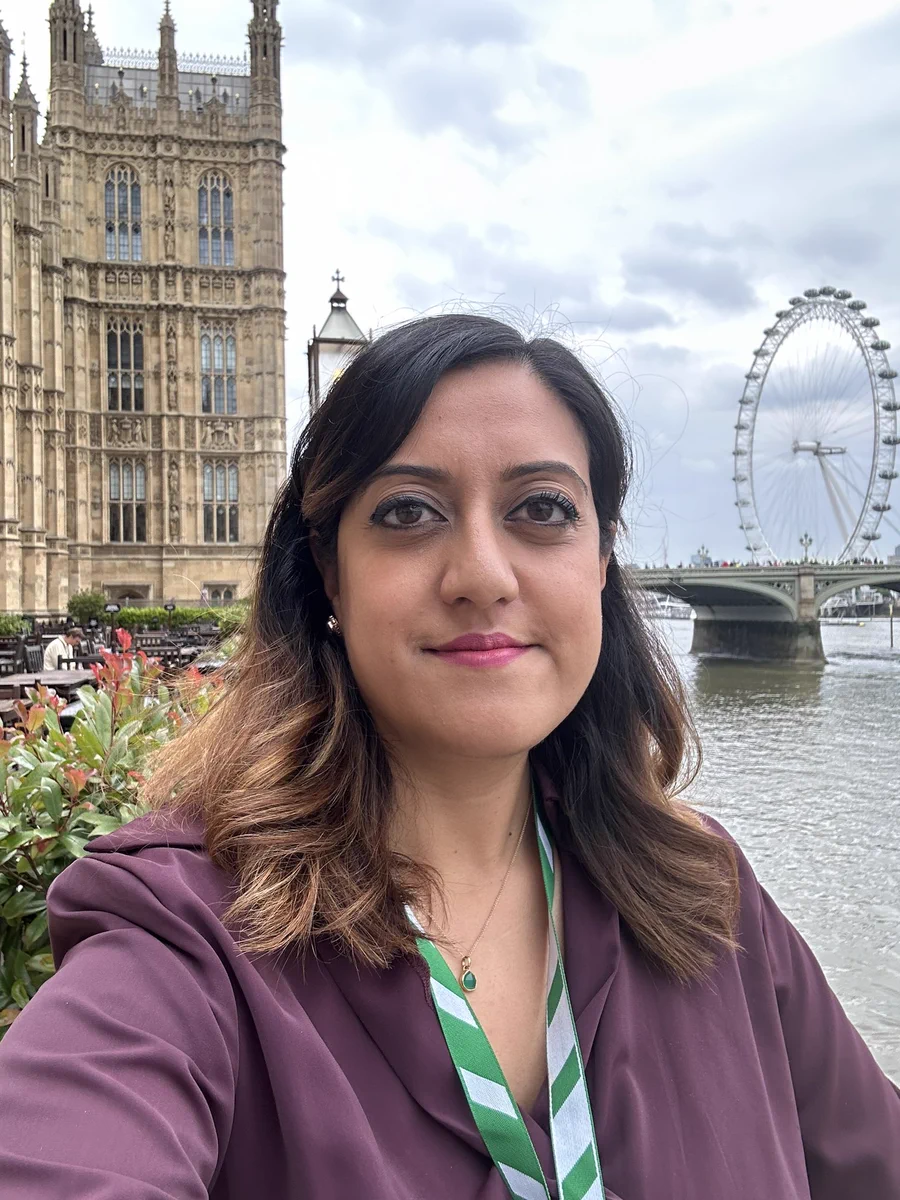 A selfie portrait of Kirith outside the Houses of Parliament with the London Eye behind